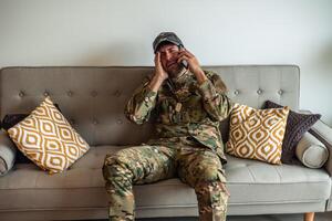 Depressed soldier crying while making a phone call at home, suffering from post-traumatic stress disorder photo
