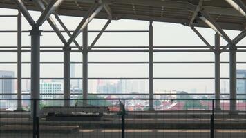 A person wearing a mask walks past a modern architectural structure with large windows, revealing a city skyline in the background. The scene conveys a sense of urban life and safety measures. video