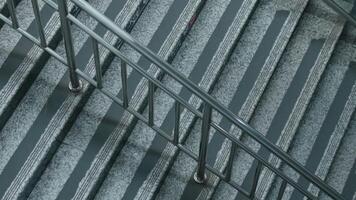 A close-up view of a staircase with a metal railing. The stairs are made of gray stone with white stripes, creating a modern and sleek appearance. The perspective captures the railing and the texture video