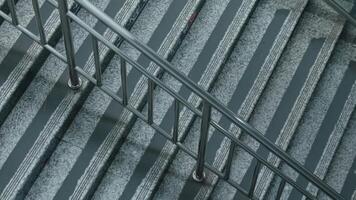A top-down view of a staircase with a metal railing. The steps are made of gray stone with alternating light and dark stripes, creating a modern architectural design. video