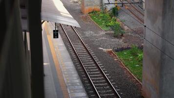 un ver de un ferrocarril pista a un tren estación, presentando vacío pistas, un plataforma borde, y verdor junto a el rieles video