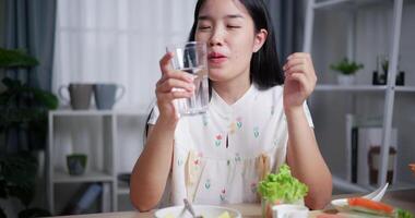 Handheld shot, Beautiful Asian woman is enjoying salad rolls and drinking water at the dining table in home. Enjoying healthy food. video