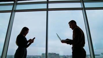 Young workers use laptop and phone in office. Business people changing their gadgets on the sky background through the windows. Business concept. video