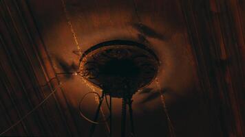 A close-up view of an ornate ceiling fixture with wires hanging down, set against a dark, textured ceiling. The lighting casts shadows that enhance the intricate details of the fixture. video