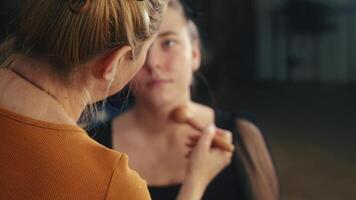Highlighter is tapped on cheekbones using a flat brush. Light dances across her skin. A subtle glow emerges video