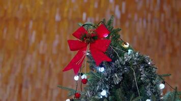 A festive Christmas tree top adorned with a bright red bow, pine cones, and colorful lights. The background features a warm, blurred texture, enhancing the holiday spirit. video
