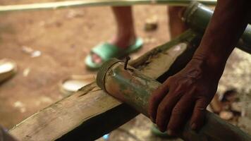 Close-up of bamboo segments being worked on, with a blurred background showing feet in green sandals. The bamboo appears freshly cut and is part of a crafting process. video