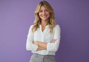 Portrait of a Confident and Smiling Woman with Blonde Hair, Wearing a White Polka Dot Blouse and Grey Pants Against a Purple Background photo