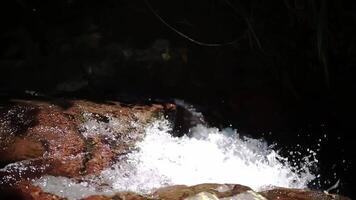 A close-up view of water cascading over a rocky surface, creating splashes and bubbles. The sunlight reflects off the water, adding a shimmering effect. video