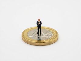 Miniature man in suit standing on top of a euro coin photo