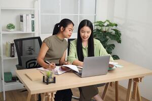 Portrait of Two Asian businesswoman are working together at a desk, discussing documents while looking at a laptop screen. photo