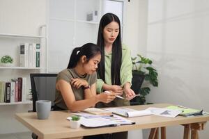 Portrait of Two female colleagues are working together in an office. A young woman is standing, talking and exchanging ideas with another colleague who is sitting. photo