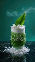 Luxurious pandan coconut milk tea in a tall double-walled glass on a reflective black countertop with teal backdrop photo