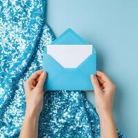 Woman's hands holding an envelope with a blank card on a blue sequinned fabric photo