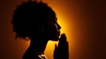 A woman in silhouette praying in front of a bright light photo