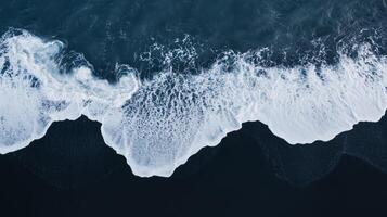 Aerial perspective of waves crashing onto a black basaltic sand beach photo