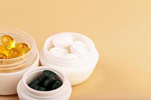 Three white jars filled with yellow capsules, white tablets and green spirulina pills arranged on beige background photo
