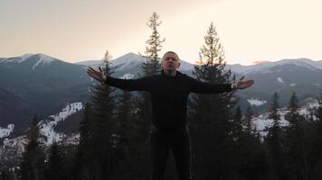Man in black standing on mountain viewpoint in winter Carpathians, sunset sky and pine trees in background video