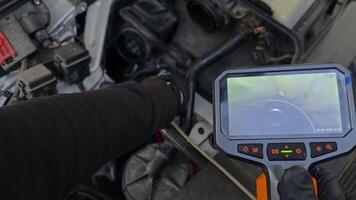 Mechanic using borescope camera to inspect engine internals, live view displayed on handheld screen video