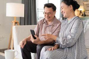 Asian sSior couple enjoy using mobile phone on sofa. grandparent learning and connecting with social media, vdo call with family, shopping online, surfing the internet. photo