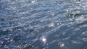 Bright sunlight gleaming and sparkling across gently flowing blue water surface, creating mesmerizing light reflections and serene natural texture. video