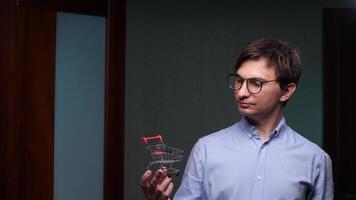 Office worker holding small shopping cart reflecting on purchases and consumerism video