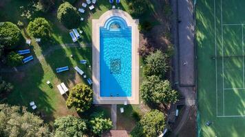 Relaxing summer afternoon by a shimmering pool in a lush garden setting, surrounded by trees and tennis courts photo