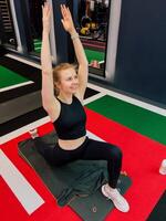 Woman doing stretch on yoga mat indoors, stretch pose shows flexibility and control, stretch emphasises active body, stretch moment captured in gym with calm smile. Fitness moment with woman on mat photo