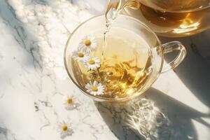 A glass teapot with a luminous stream of chamomile tea arching gracefully into a glass cup. photo