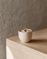 A matte ceramic cup with iced coffee on a light birchwood surface. Decorated with a single coffee bean on the foam. photo