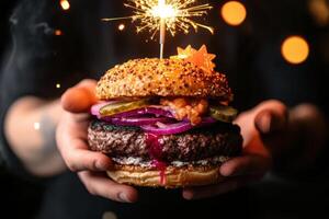 Male hands cradle a towering gourmet burger designed as a birthday cake. A single sparkler replaces the classic birthday candle, sending up glittering embers that blend with the city lights. photo
