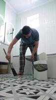 A man in home clothes sweeping the floor in the bathroom, using garbage bin video