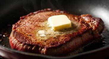 A juicy steak sizzles in a hot skillet, topped with a melting pat of butter photo