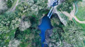 Waterfall cascades over rocks into a serene blue pool embraced by lush greenery in a tranquil forest setting photo