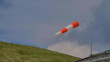 Wind direction indicator waves gracefully above a lush green hillside under a clouded sky in a serene rural setting photo