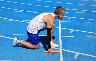 Senior Asian athlete is practicing running block start in professional blue track for professional exercise, sport training workout and healthy for longevity photo