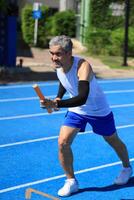 Senior Asian athlete is practicing running with the relay baton in the professional blue track for professional exercise, sport training workout and healthy for longevity concept photo