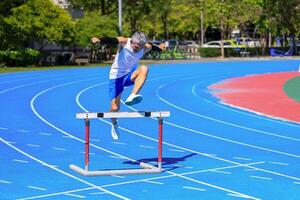 Asian senior athlete is practicing hurdling running in the professional blue track for professional exercise, sport training workout and healthy for longevity photo