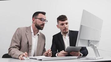Two business men are brainstorming in a bright office, working and analyzing data from a computer. The concept of successful business and teamwork video