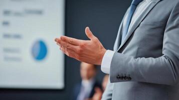 Cropped view of businessman in gray suit gesturing with hand during presentation, with blurred chart or graph in background photo