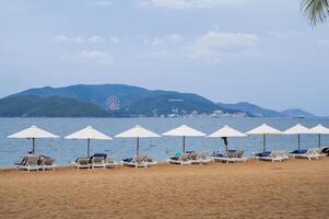 sandy beach with tourists relaxing under beach umbrellas by sea in Nha Trang resort in Vietnam in summer cloudy day photo