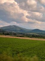 Green field stretching towards majestic mountains under cloudy sky photo