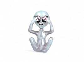 An alien figurine sitting on the floor with its hands over its eyes photo