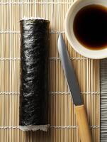 Preparing sushi with a sharp knife on a bamboo mat alongside a bowl of soy sauce for dipping photo