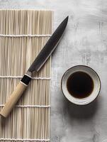 Expert sushi preparation tools featuring a bamboo mat, sharp sushi knife, and a bowl of soy sauce photo