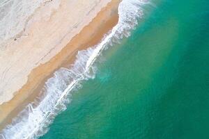 sandy beach with breaking waves and foam from above, aerial drone zenithal photography photo