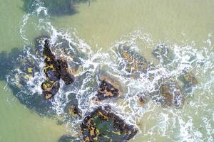 aerial view of beach rocks with wave breaking aerial perspective of natural rock texture on a sandy beach with approaching and breaking waves photo