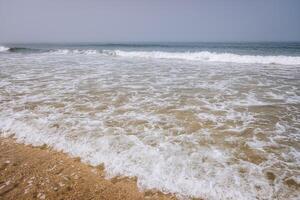 Serene beach scene with a calm ocean and overcast sky. detail of a wave breaking on a sandy shore photo