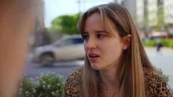 Young woman engaging in animated conversation at outdoor cafe, displaying nuanced facial expressions ranging from serious contemplation to warm, genuine smile during relaxed social interaction video