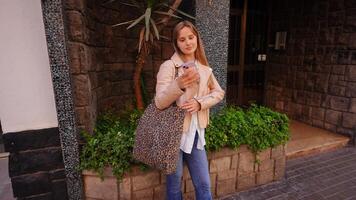 joven de moda mujer capturar selfies con teléfono inteligente mientras posando dinamicamente a lo largo urbano ciudad calle, exhibiendo confidente moderno estilo de vida y social medios de comunicación contenido creación video